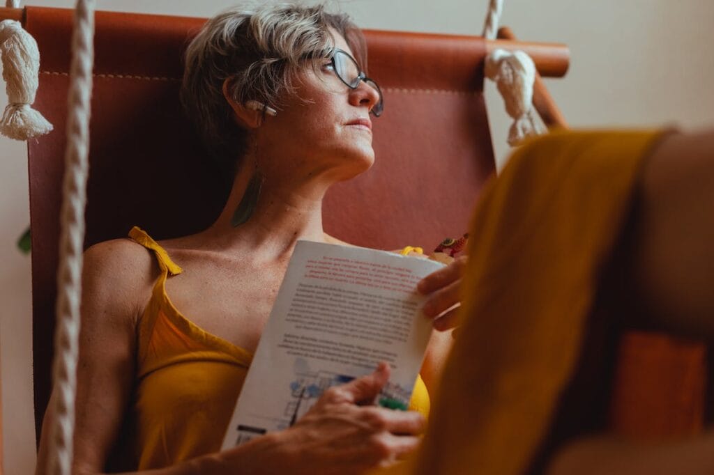 Žena s fibromyalgiou číta knihu v hojdacej sieti.