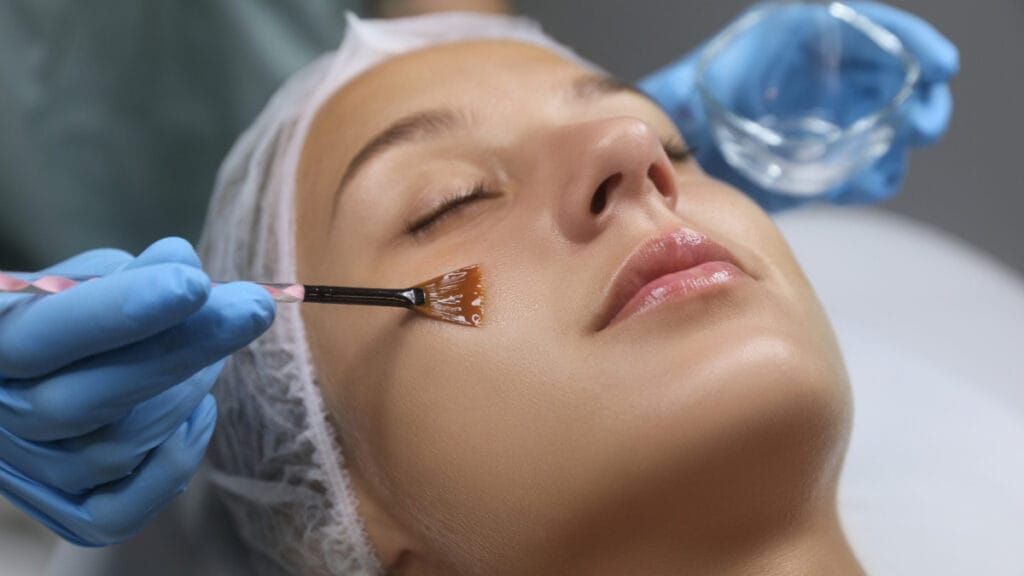 Žena, ktorá zažíva v salóne krásy účinný postup ošetrenia tváre, ktorého súčasťou je chemický peeling pre umocnený omladzujúci zážitok.