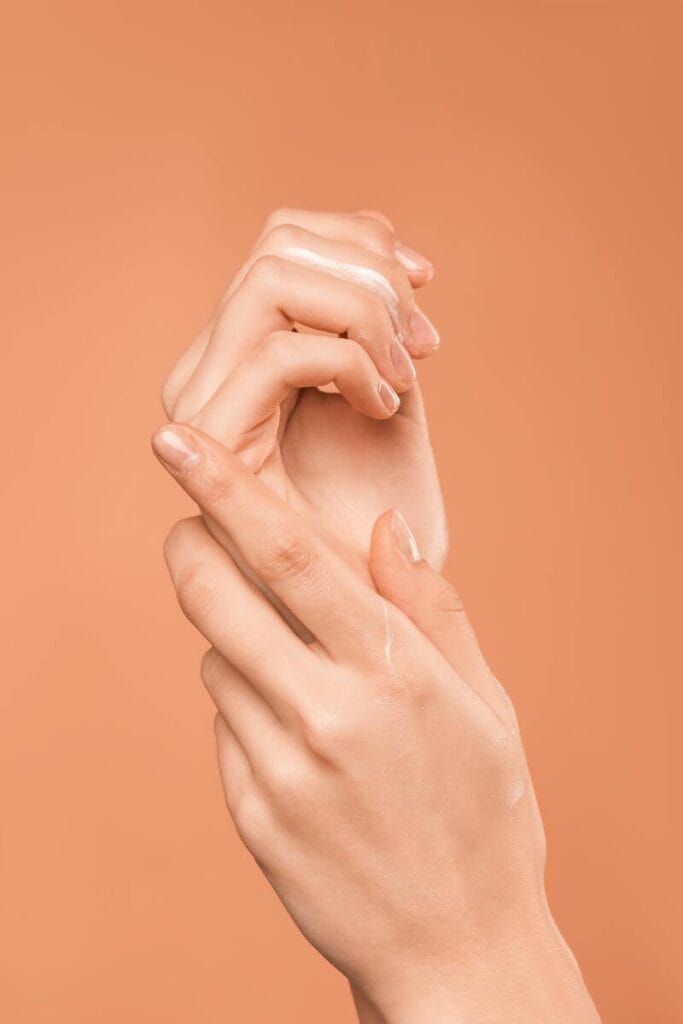 Ženské ruky držia krém na oranžovom pozadí. Pleťová voda je známa svojou schopnosťou zlepšovať krvný obeh a poskytuje úľavu od bolesti.